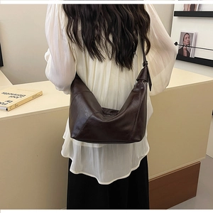 Detail of dark brown leather crescent bag showing soft pleats and modern shoulder strap