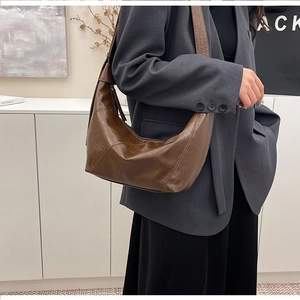 Side view of brown leather hobo bag with adjustable strap worn by model in suit