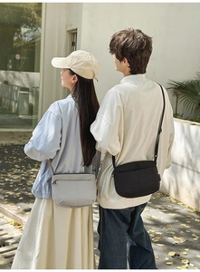 Photo en extérieur d'un sac bandoulière minimaliste en nylon crème et noir avec sangle