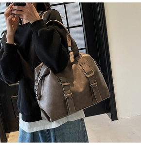 Detail of a large brown faux leather tote bag featuring retro buckles and wide shoulder straps