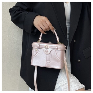 Detail of light pink box bag showing quilted texture and gold clasp on black suit