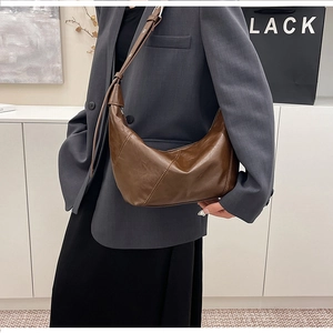 Brown leather crescent bag worn over a grey blazer showing its size and drape