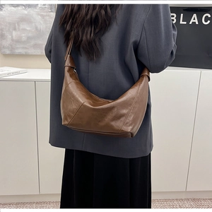 Detail of a dark brown glossy hobo bag shown from the back on a model for daily styling