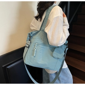 Detail view of light blue nylon tote bag showing woven zipper pull and crossbody strap