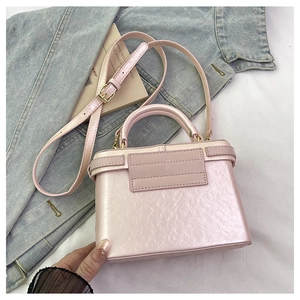 Detail of a light pink pearlescent box bag with adjustable strap on denim jacket