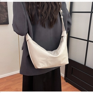 Minimalist ivory hobo bag worn over shoulder, showing sleek leather texture and strap detail