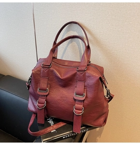 Detail of burgundy textured leather tote bag with silver hardware on black sofa