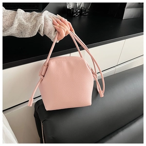 Detail view of pink pebbled leather handbag with trapezoid shape and slim handles