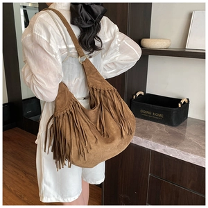 Close-up of brown suede tote bag featuring bohemian tassels and gold ring details