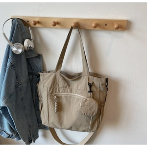Detail of khaki nylon tote bag featuring front zipper pocket and side elastic pocket