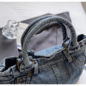 Dettaglio della borsa tote in denim blu con manici rinforzati, rivetti e cuciture a contrasto