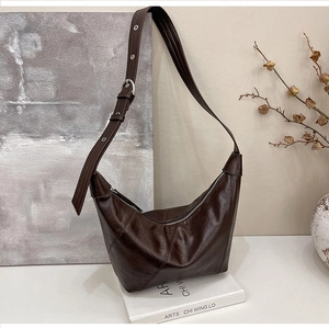 Close-up of dark brown crescent bag with polished faux leather and adjustable silver buckle