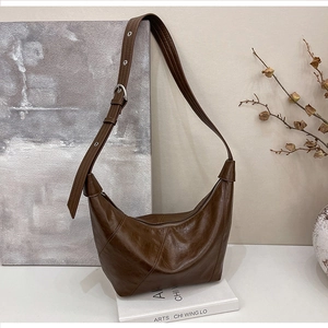 Close-up of a retro dark brown matte leather crescent bag with visible stitching and metal buckle