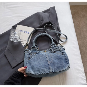Dettaglio della borsa tote in denim vintage con rivetti e cuciture su sfondo grigio