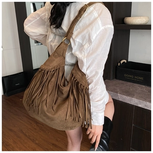 Detail of dark brown suede shoulder bag featuring long tassels and gold metal ring hardware