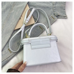 Detail of a white faux leather box bag with light gold hardware and matching shoulder strap