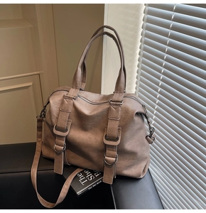 Detail of coffee PU leather Boston bag with belt buckles and dual handles on a sofa