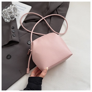 Close-up of pink lychee grain leather shell bag with zipper and knot detail on a grey blazer