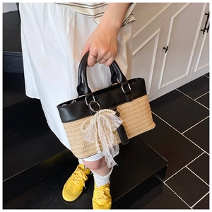 Detail of hand-woven straw tote bag with black leather stitching and pearl bow pendant