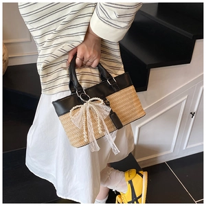 Detail of straw tote bag featuring black leather trim and lace pearl bow charm