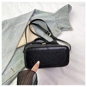 Detail shot of the black embossed leather base and adjustable strap of this square bag