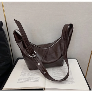 Detail of dark brown dumpling bag with wide strap and silver buckle on vintage book
