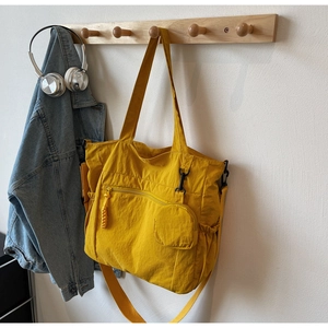 Detail of a bright yellow nylon tote bag featuring side pockets and a small attached pouch