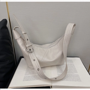 Detail of a creamy white leather crescent bag with adjustable wide strap on a book