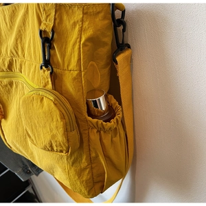 Detail of yellow nylon tote bag featuring side bottle pocket and matte black hook