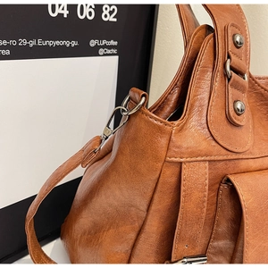 Detail of vintage brown leather handbag featuring silver rivets and metal strap hooks