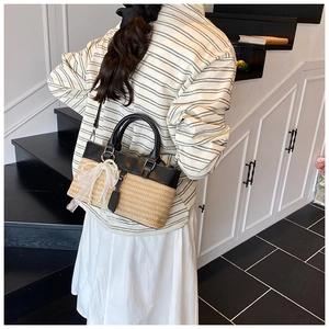 Detail of straw woven bucket bag with black leather trim and lace bow on a model