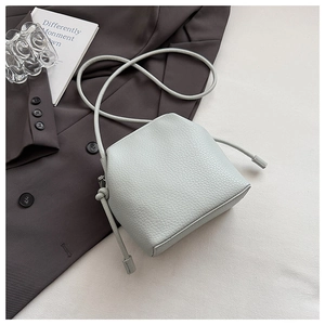 Detail of light green litchi grain leather bucket bag with drawstring on grey blazer