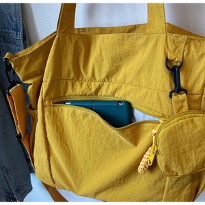 Detail of yellow nylon tote bag featuring front zipper pocket and round coin purse attachment