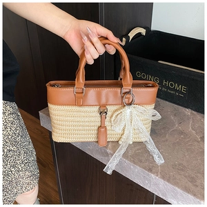 Detail of the woven straw tote bag with brown leather trim and a white lace bow charm