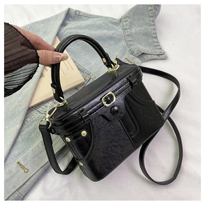 Close-up of black textured leather box bag with gold rivets and sturdy round handle