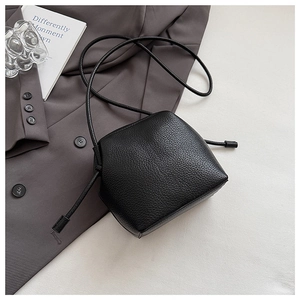 Detail of black lychee grain leather crossbody bag on a stylish grey blazer jacket