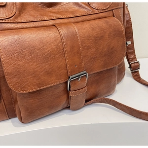 Close-up of brown PU leather shoulder bag featuring a metal buckle and fine texture