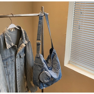 Detail of blue washed denim crossbody bag featuring a round coin purse and wide strap