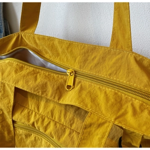 Detail shot of the bright yellow nylon tote bag featuring smooth metal zipper and durable seams
