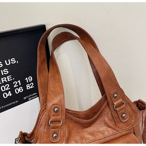 Close-up of brown textured leather handbag with metal rivets and D-ring strap hardware