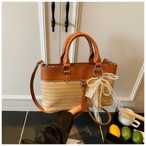 Close-up of woven straw tote bag with brown leather trim and pearl lace bow detail