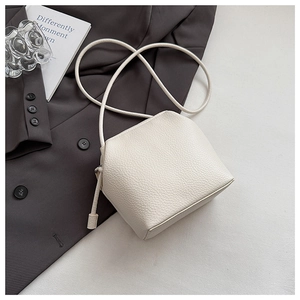 Detail of off-white lychee grain leather crossbody bag on a grey suit with modern styling