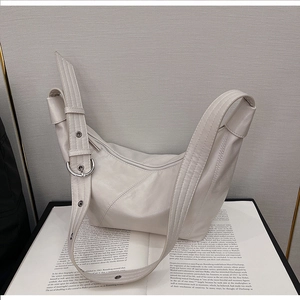 Detail of cream hobo bag with pebble leather texture and silver buckle on an open book
