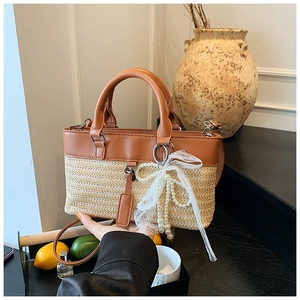 Detail of straw tote bag with brown leather handles and decorative pearl lace bow