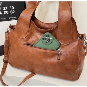 Brown soft leather tote bag showing detail of a green phone being placed in the front zip pocket
