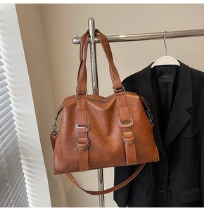 Detail view of brown textured PU leather tote bag with stylish metal buckles and long strap