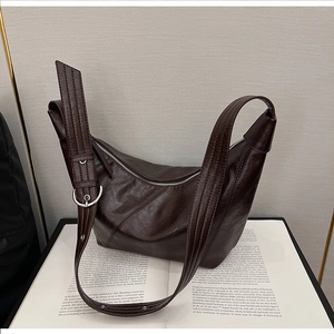 Detail of a minimalist dark brown leather dumpling bag placed on an open art book