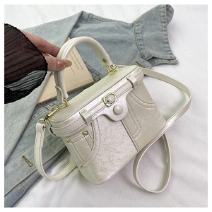 Detail of a pearlescent white box bag with gold metal lock and elegant top handle