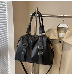 Detail of black textured tote bag featuring metallic buckles and adjustable shoulder strap