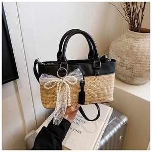 Detail of straw tote bag with black leather trim, lace bow, and pearl decoration